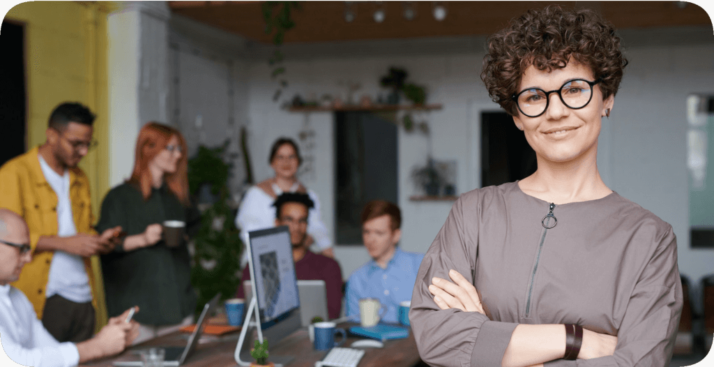 Woman in glasses stands in front of colleagues.